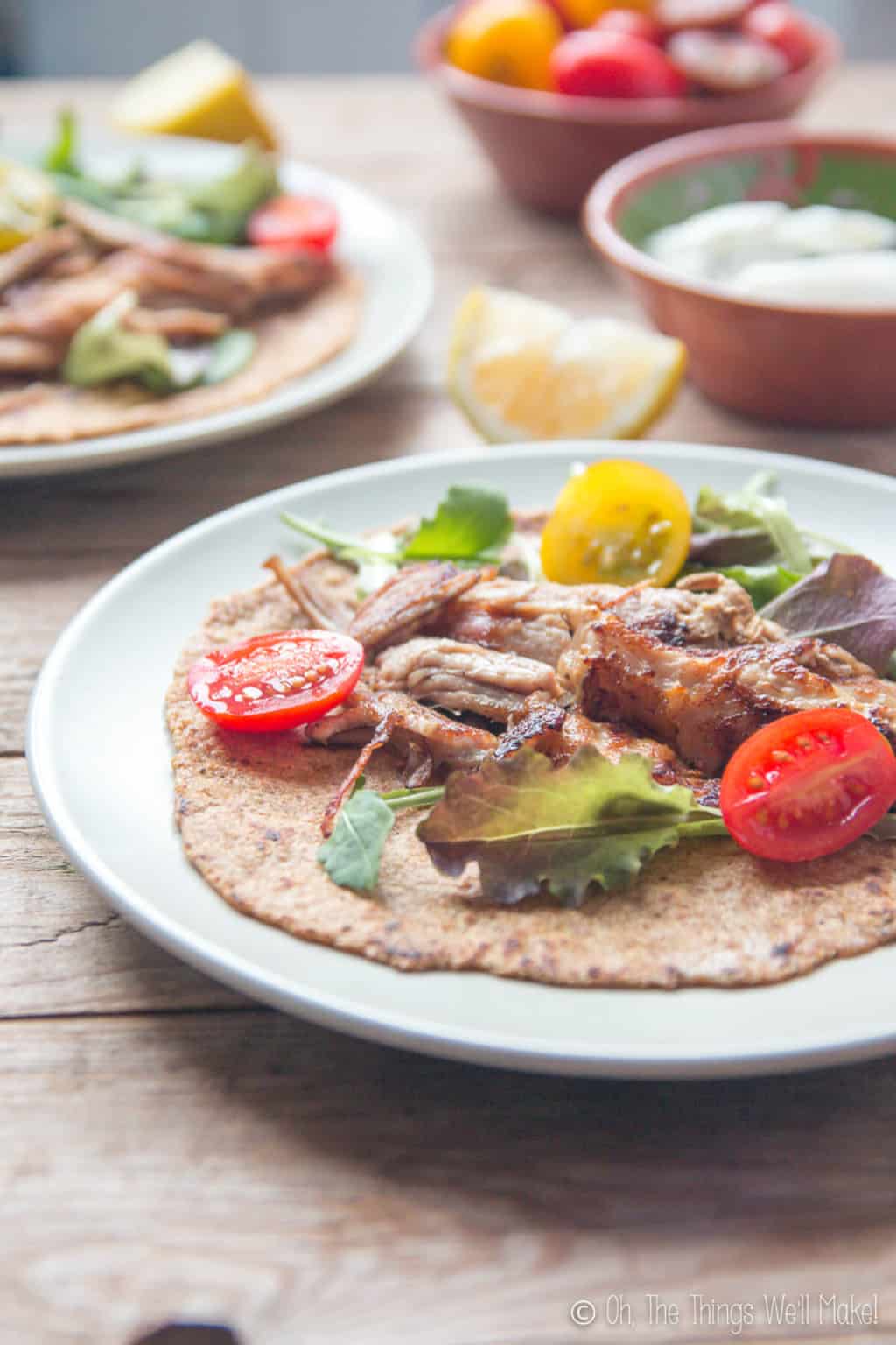 Closeup of plates with crispy pork carnitas with sliced open cherry tomatoes and lettuce on a flaxseed tortilla.