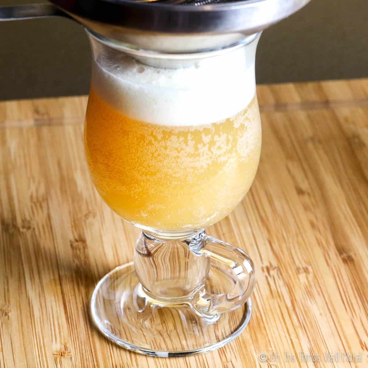 A black strainer over a glass full of kefir apple cider. 