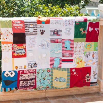 A colorful keepsake quilt made out of old baby clothes placed on a balcony balustrade.