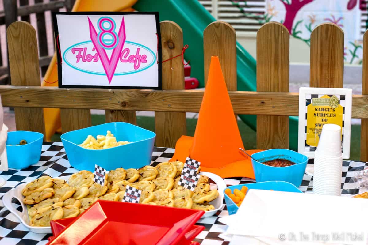 Spanish "cocas" on a table with other snack foods on a table covered in checkered tablecloth, next to a sign that says "Flo's Cafe" and next to an orange craft foam cone. 