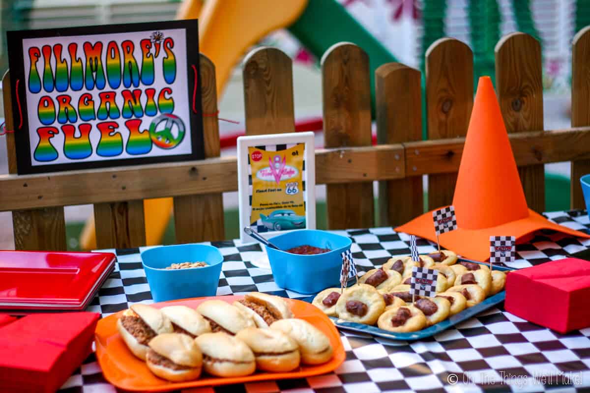 Sandwiches and other snack foods on a table covered in checkered tablecloth, next to an orange cone made from craft foam, and a sign that says "Fillmore's organic fuel"
