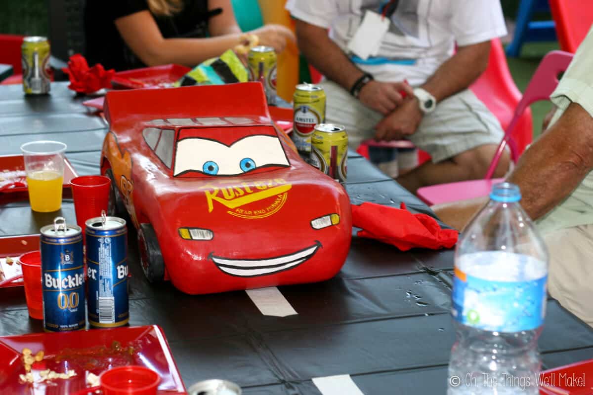 A paper mache "Lightning McQueen" on a table with a black tablecloth marked with a white dashed line made out of masking tape (to represent a road). 