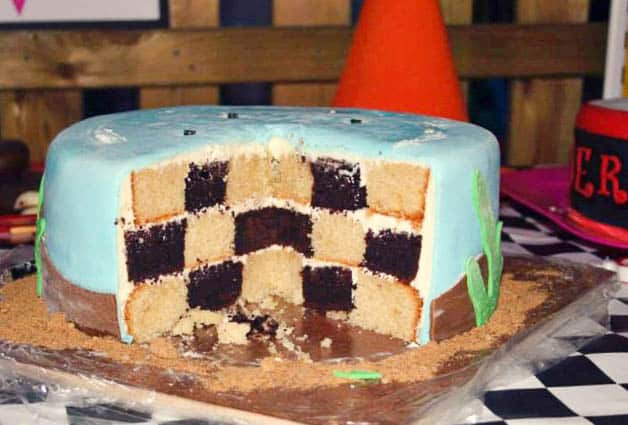 A cut cake showing a checkerboard interior made with white and chocolate cakes.