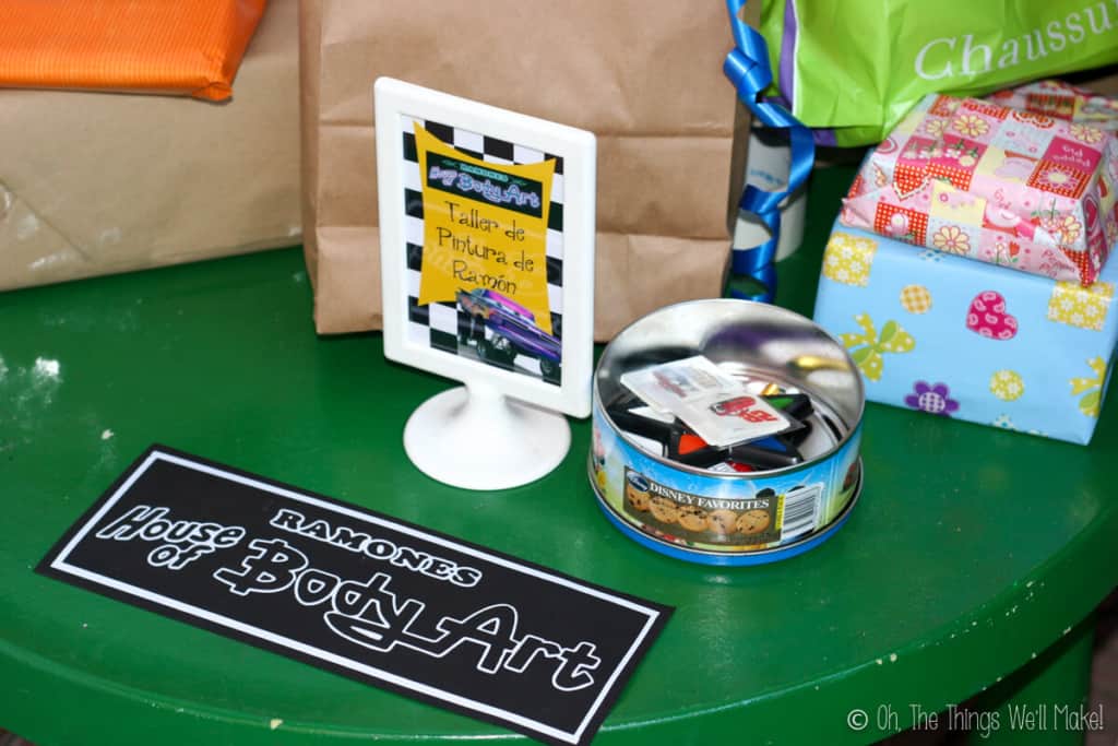 A sign that says "Ramone's House of Body Art" next to a tin filled with temporary tattoos and face paint.