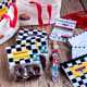Car themed items: white and red little tote bags, VIP pit pass invitations with red lanyard, Chocolate donut party treats, kid watch, and coloring books laid on a wood surface.