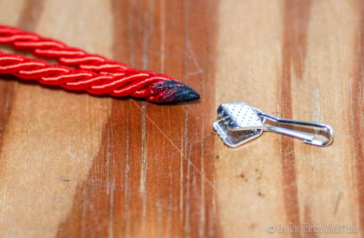 Closeup of the burned points of red cording together, next to a lanyard clip.
