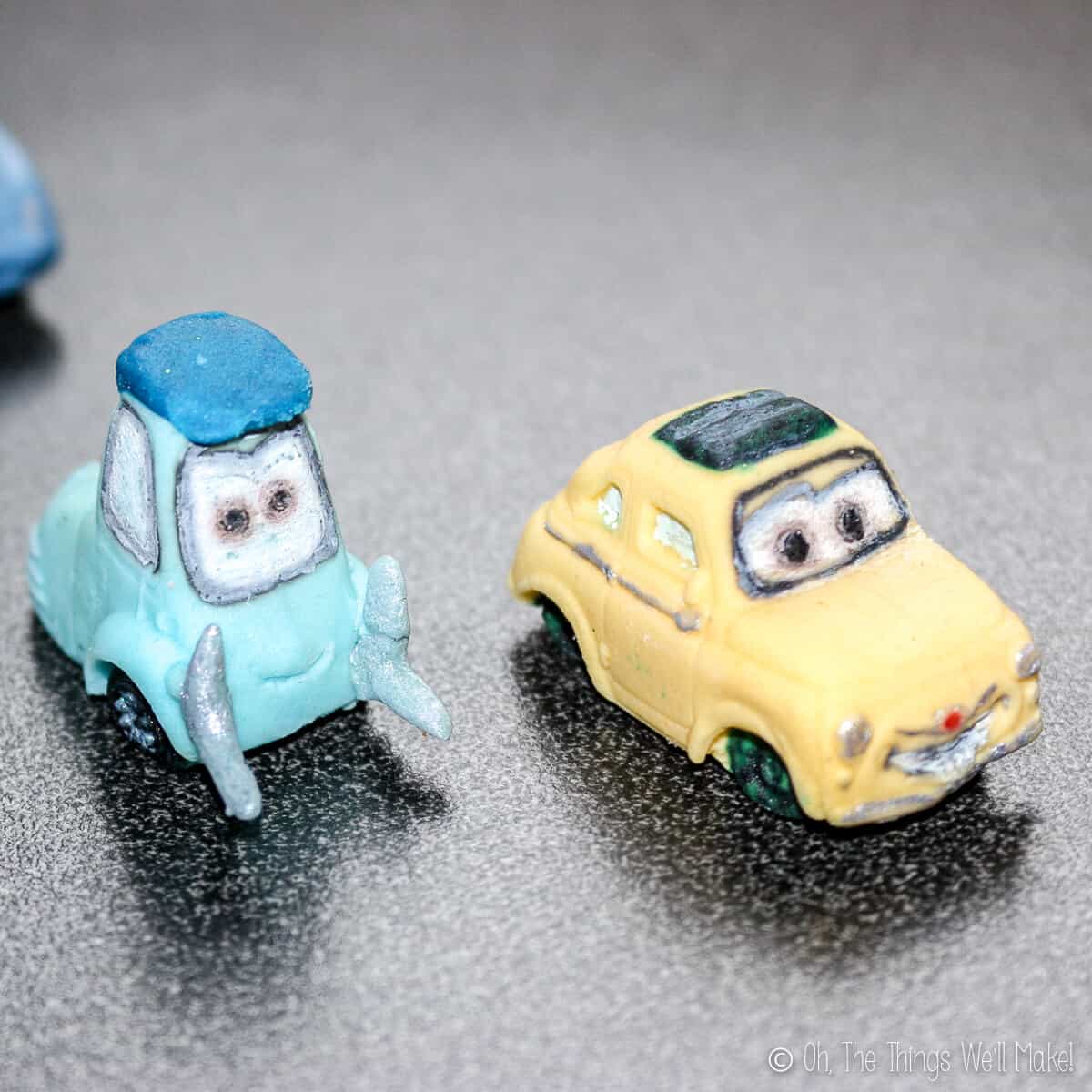 Close up of two fondant car decos: light blue Luigi and yellow Guido.