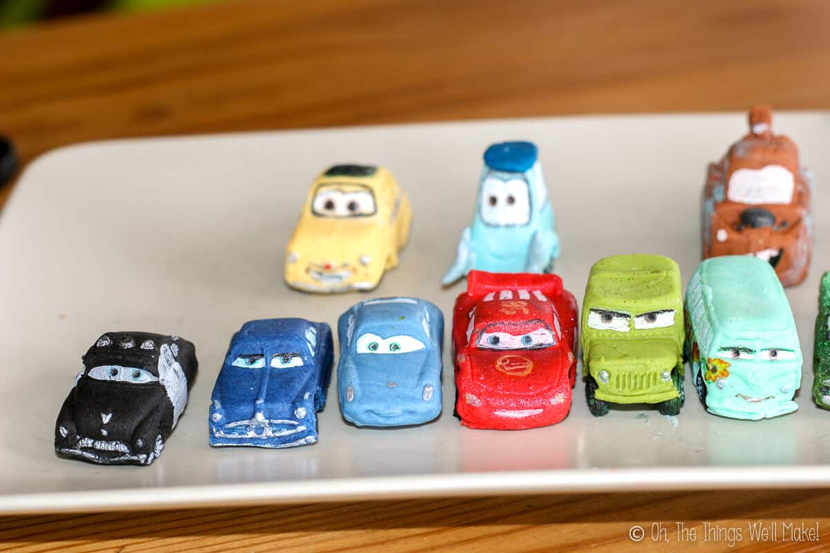 Eleven different cars from the Disney Pixar Cars movies made from fondant laid on a white plate.