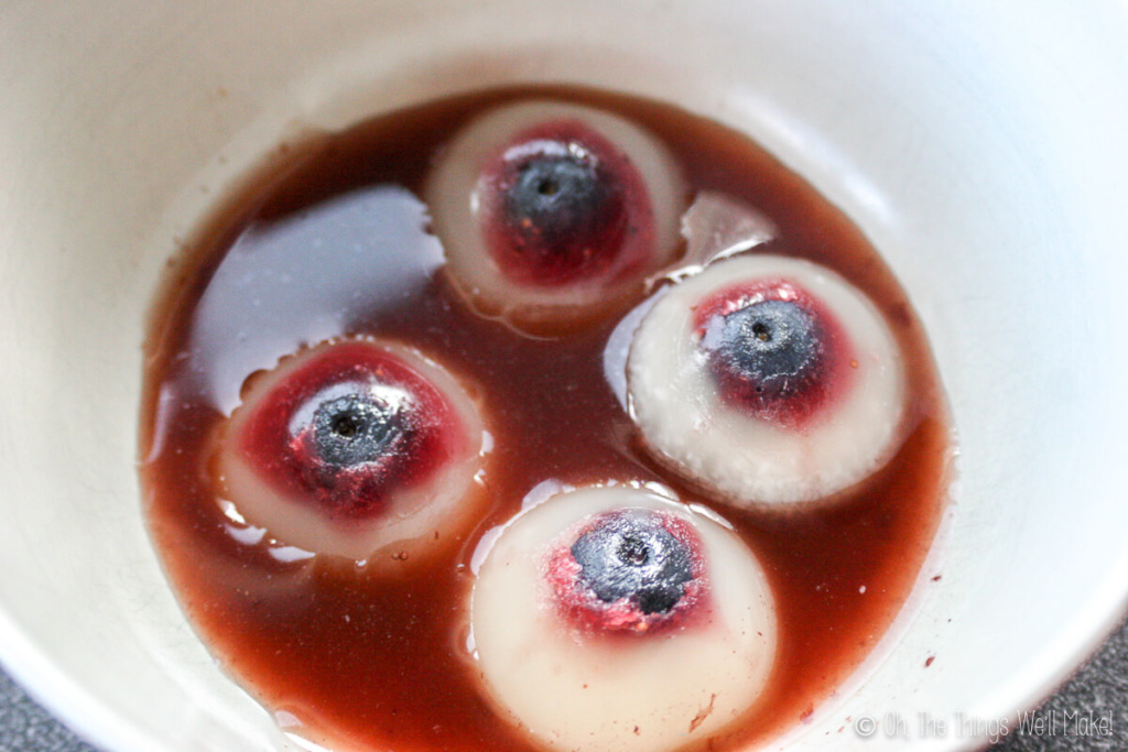 Four gummy eyeballs shown in a bowl served in red fruit juice.