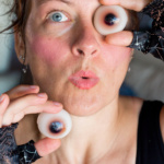 A woman holding up two homemade gummy eyeballs: one against one of her eyes and the other below her face.