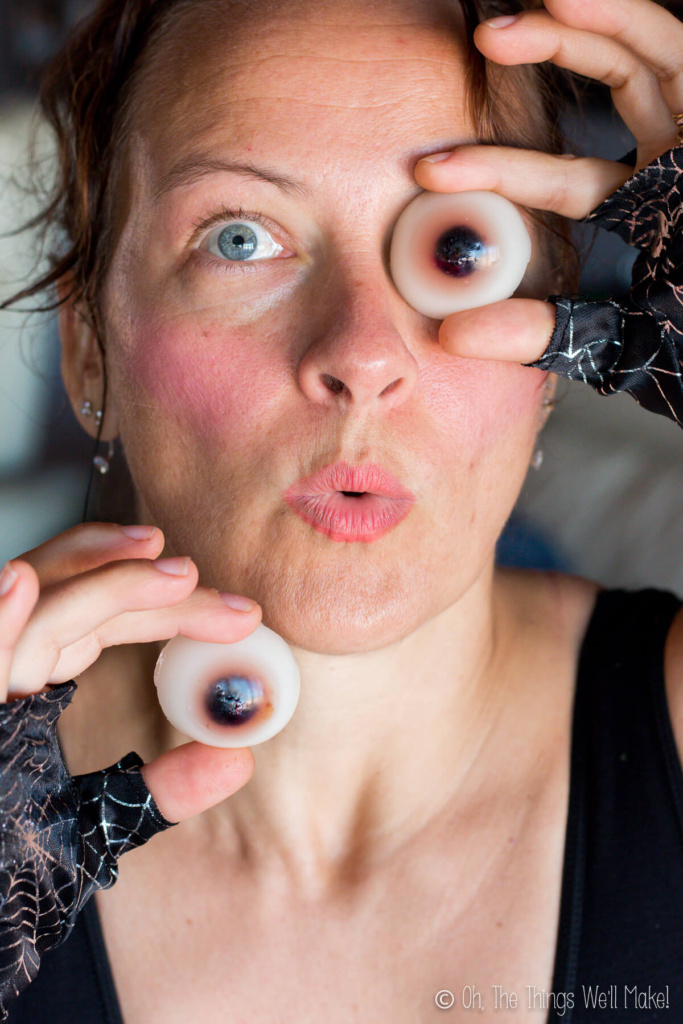 A woman holding up two homemade gummy eyeballs: one against one of her eyes and the other below her face.