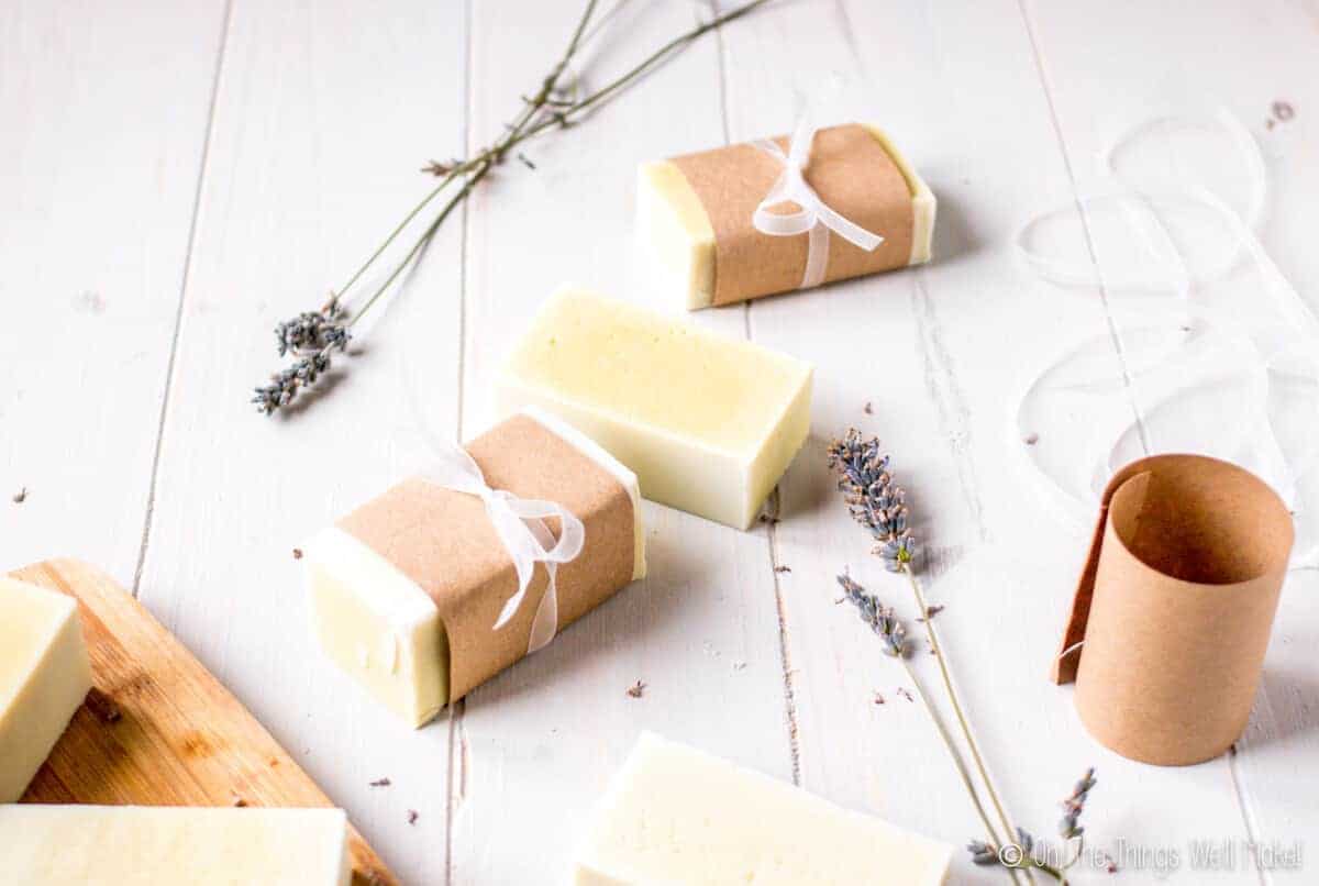 Homemade soap, surrounded by lavender flowers, wrapped with paper and ribbons. Some paper and ribbon are seen on the side.