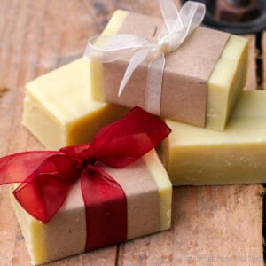 Closeup of 4 bars of homemade soap. Two of them have been wrapped in brown paper and wrapped with ribbons. One soap is wrapped with red ribbon and the other with white ribbon.