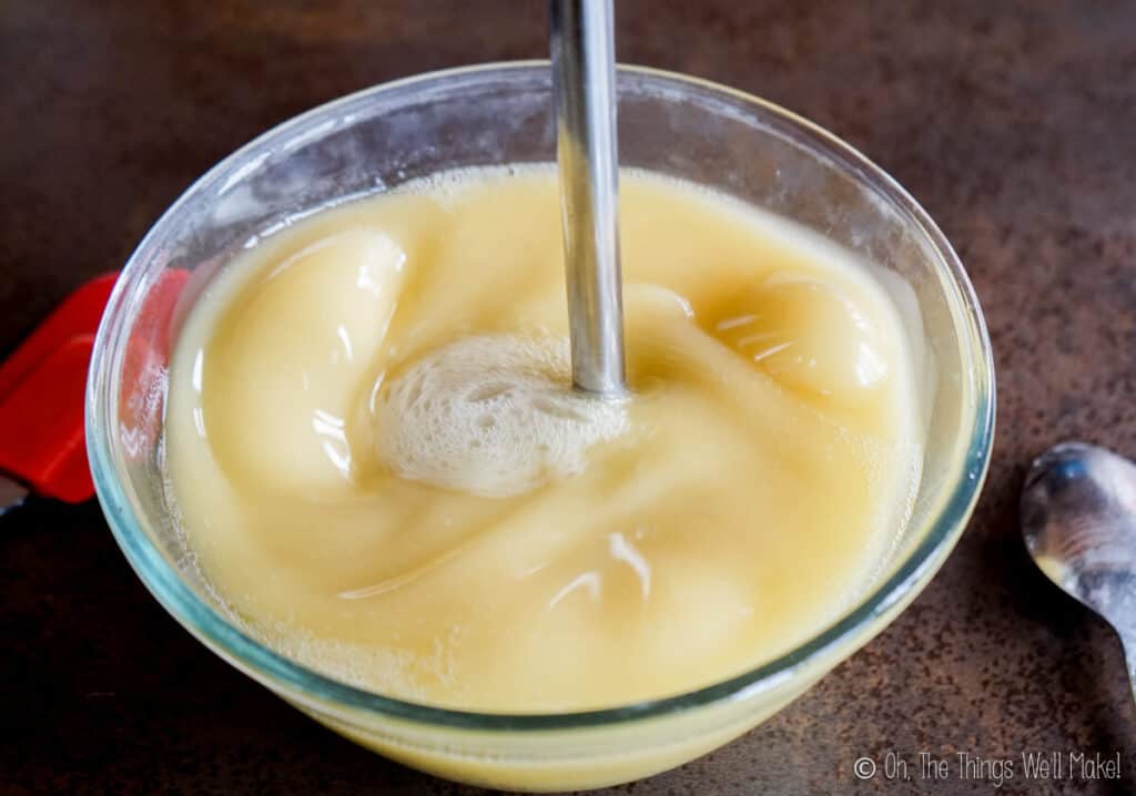 An immersion blender being used to blend the soap mixture in a large bowl.