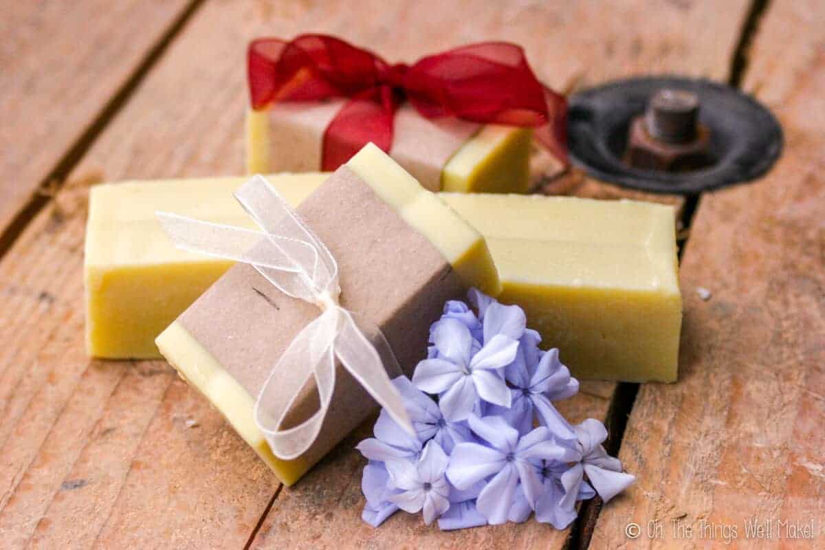 4 bars of homemade soap by some blue flowers. Two are wrapped in paper.