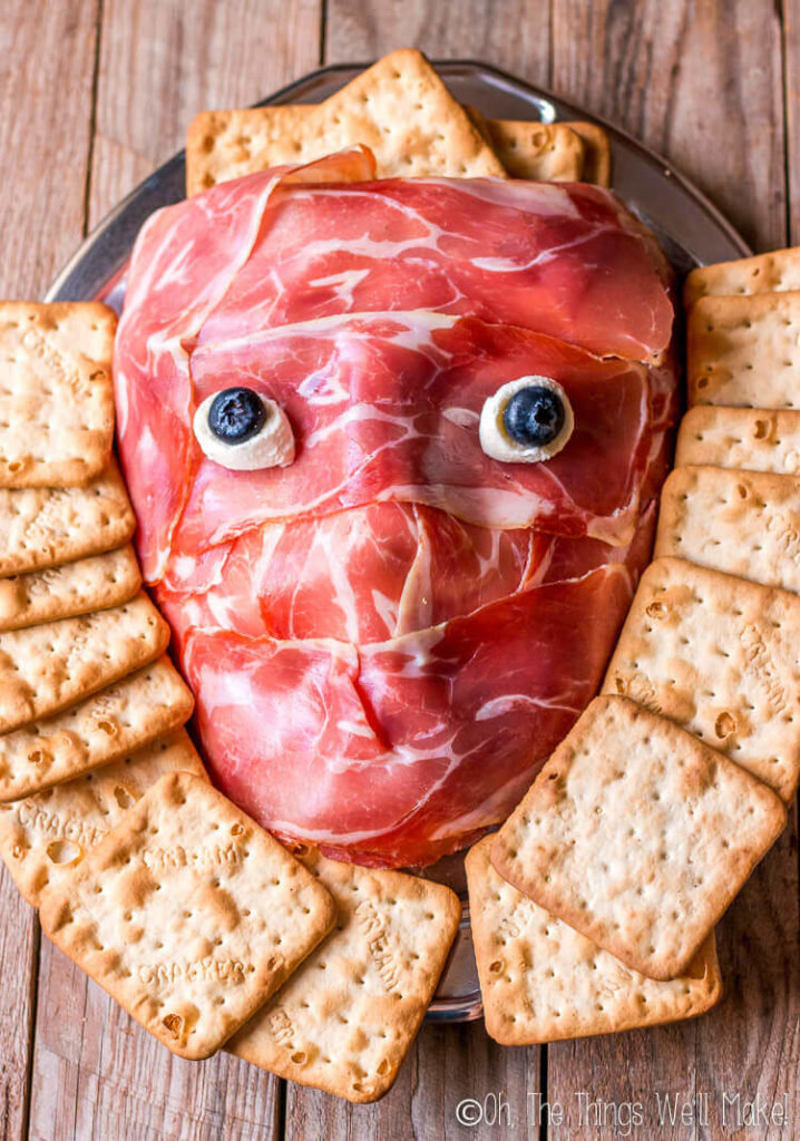 Overhead view of a prosciutto face on a platter, surrounded by crackers.