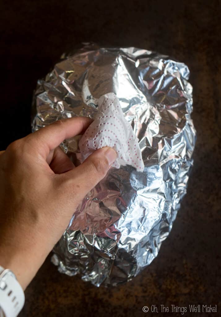 Oval spheroid covered in aluminum foil with another ball of paper sitting on top where the nose should be.
