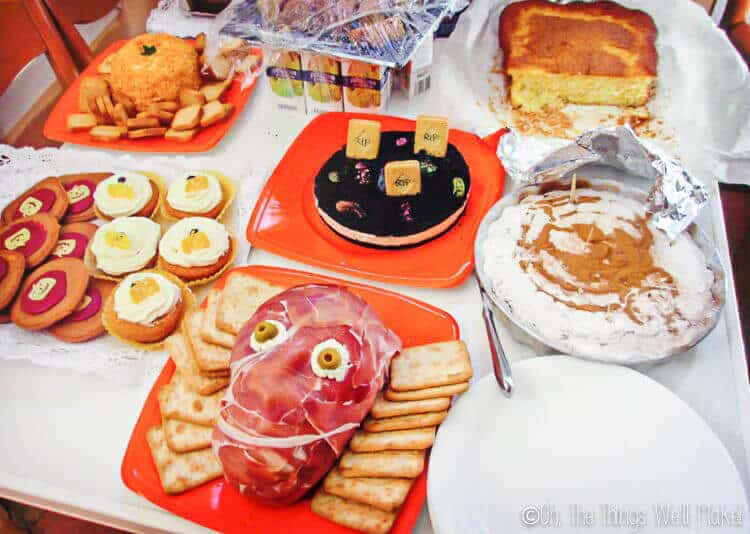 Table with Halloween foods including a prosciuttos face and a pumpkin shaped cheeseball with crackers