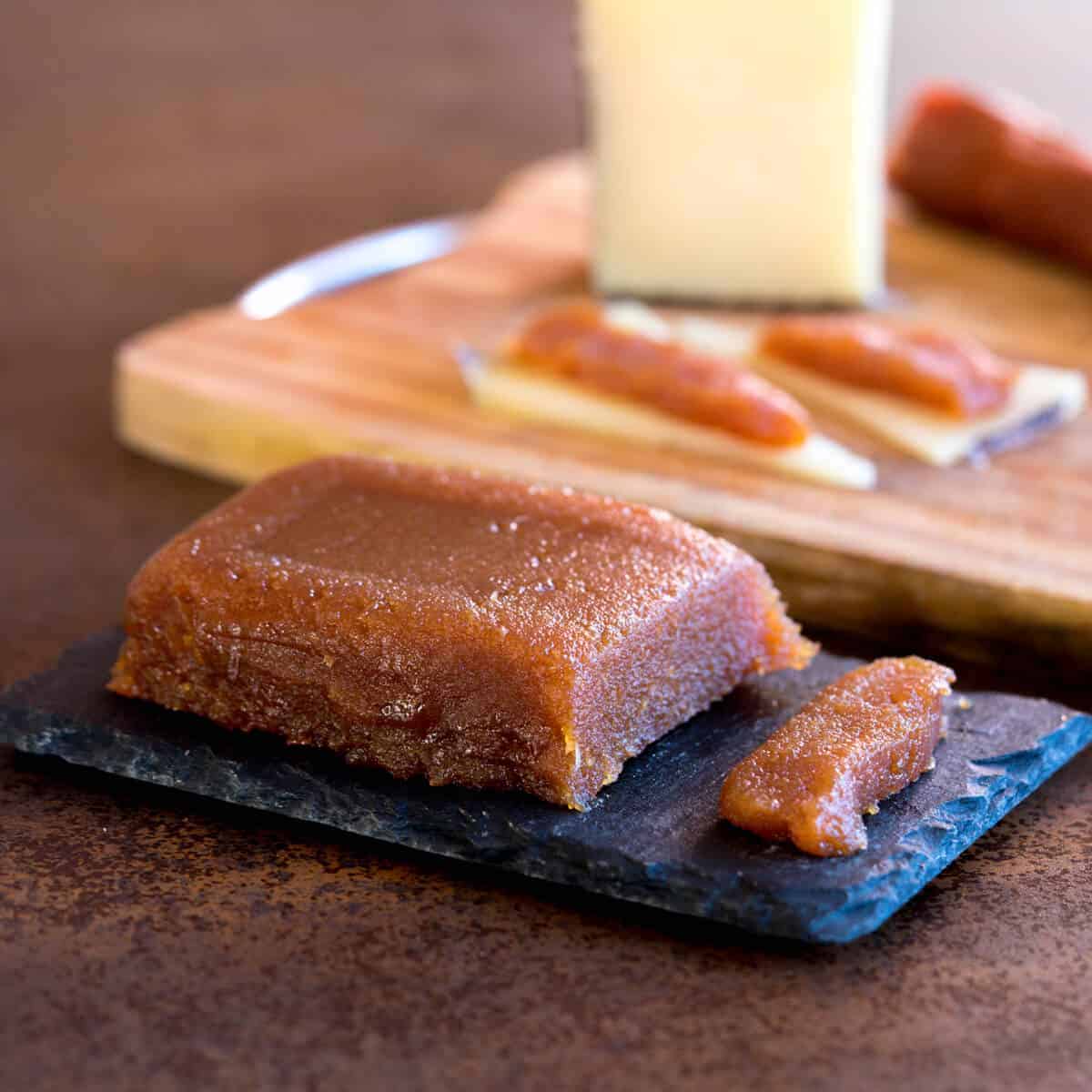 a homemade membrillo (quince paste) on a platter, in front of a cutting board with manchego cheese and chorizo sausage.