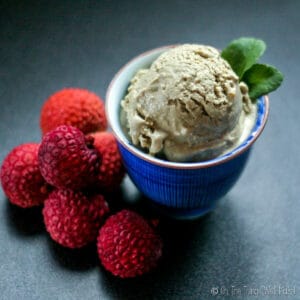 Closeup of a homemade green matcha lychee ice cream in a blue bowl with red lychees around the bowl.