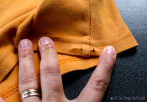 Small slits have been cut into the bottom hem enclosure of the t-shirt on either side of the seam
