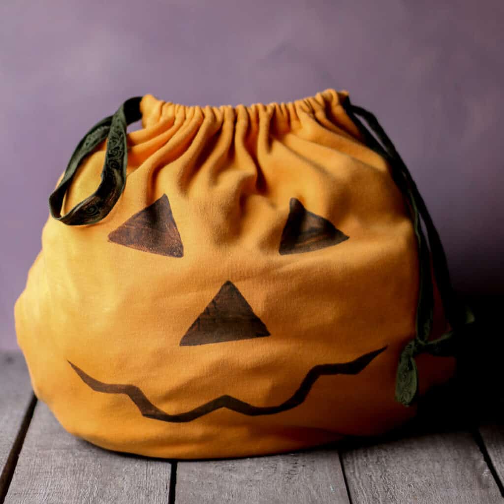 An orange homemade trick-or-treat bag decorated with a Jack-o-lantern face.