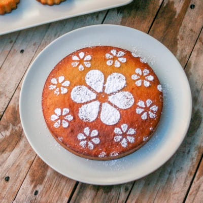 Overhead view of a golden brown circle spanish almond cake decorated with powdered sugar in floral shapes.