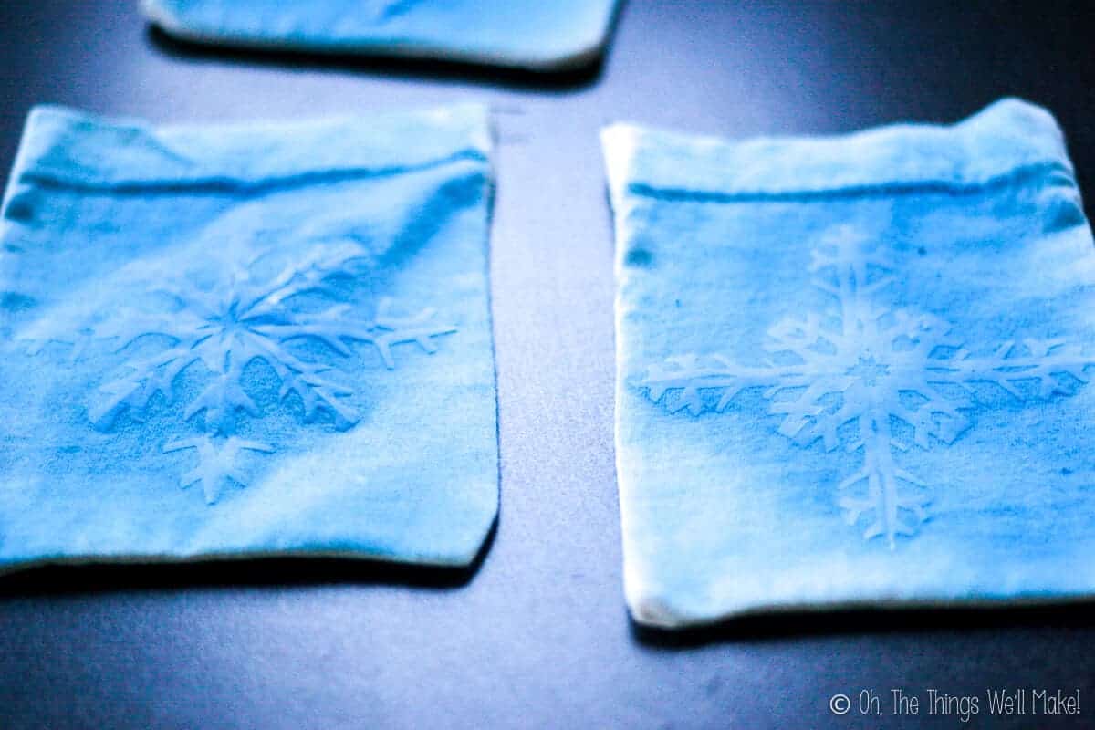 Two pouches with freezer paper snowflakes ironed on the front, that have been painted blue.
