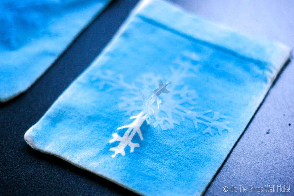 lifting up the edge of one of the freezer paper snowflakes, revealing a white snowflake underneath.