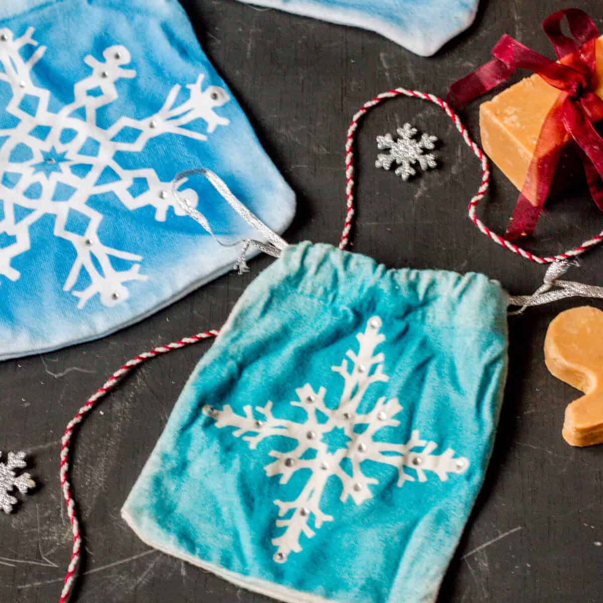 Two homemade blue cloth gift pouches with painted snowflakes designs and embellished with rhinestones.