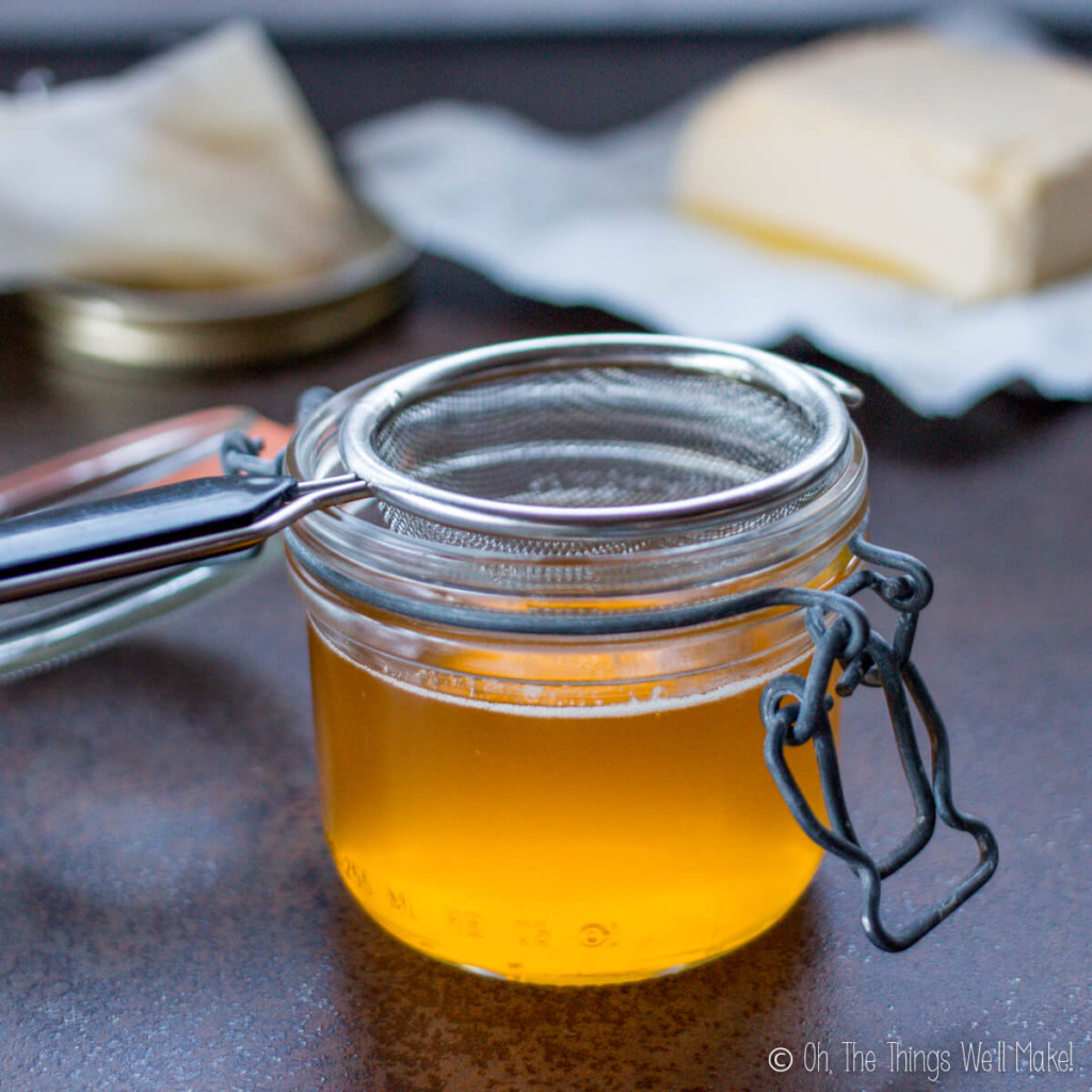 Close-up of a container full of yellow ghee oil and a block of butter in the background.