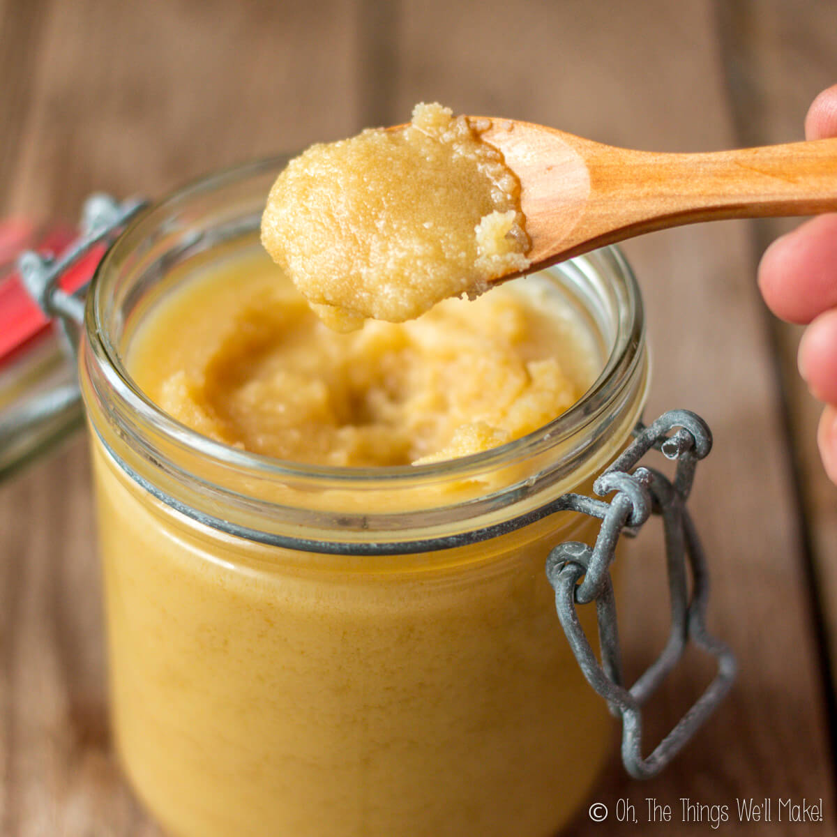 a jar of ghee with a spoonful of ghee held up over it to show texture