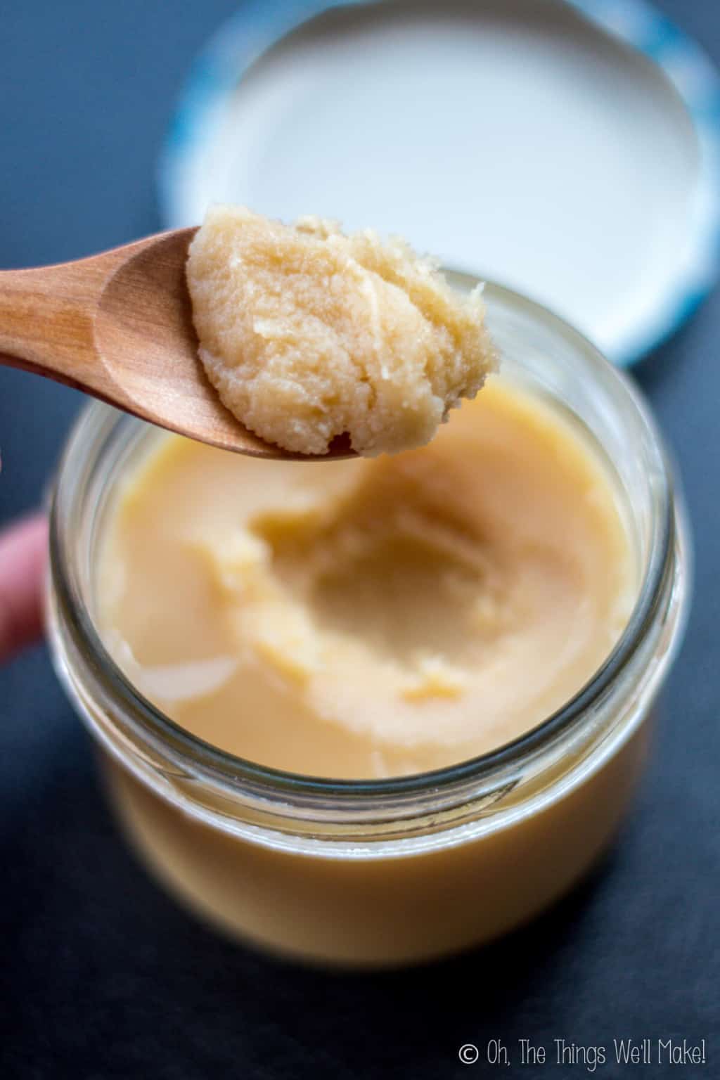 Close up of a wooden spoon full of solid ghee held over an open jar filled with ghee kept in the refrigerator.