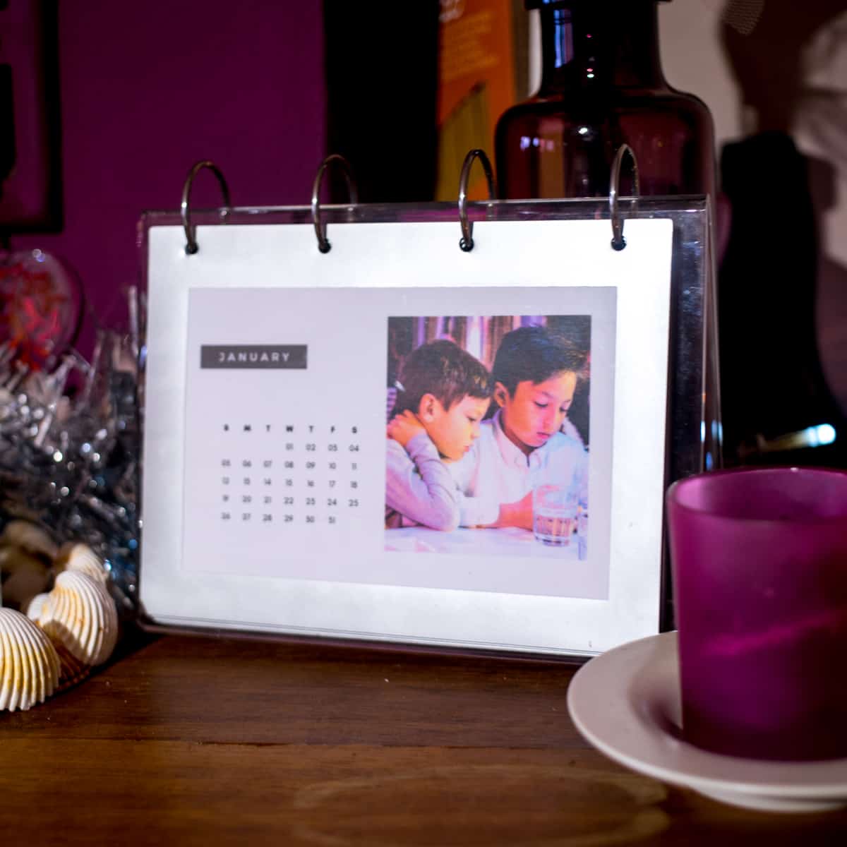 A homemade photo calendar sitting on a mantle with some candles and other trinkets.