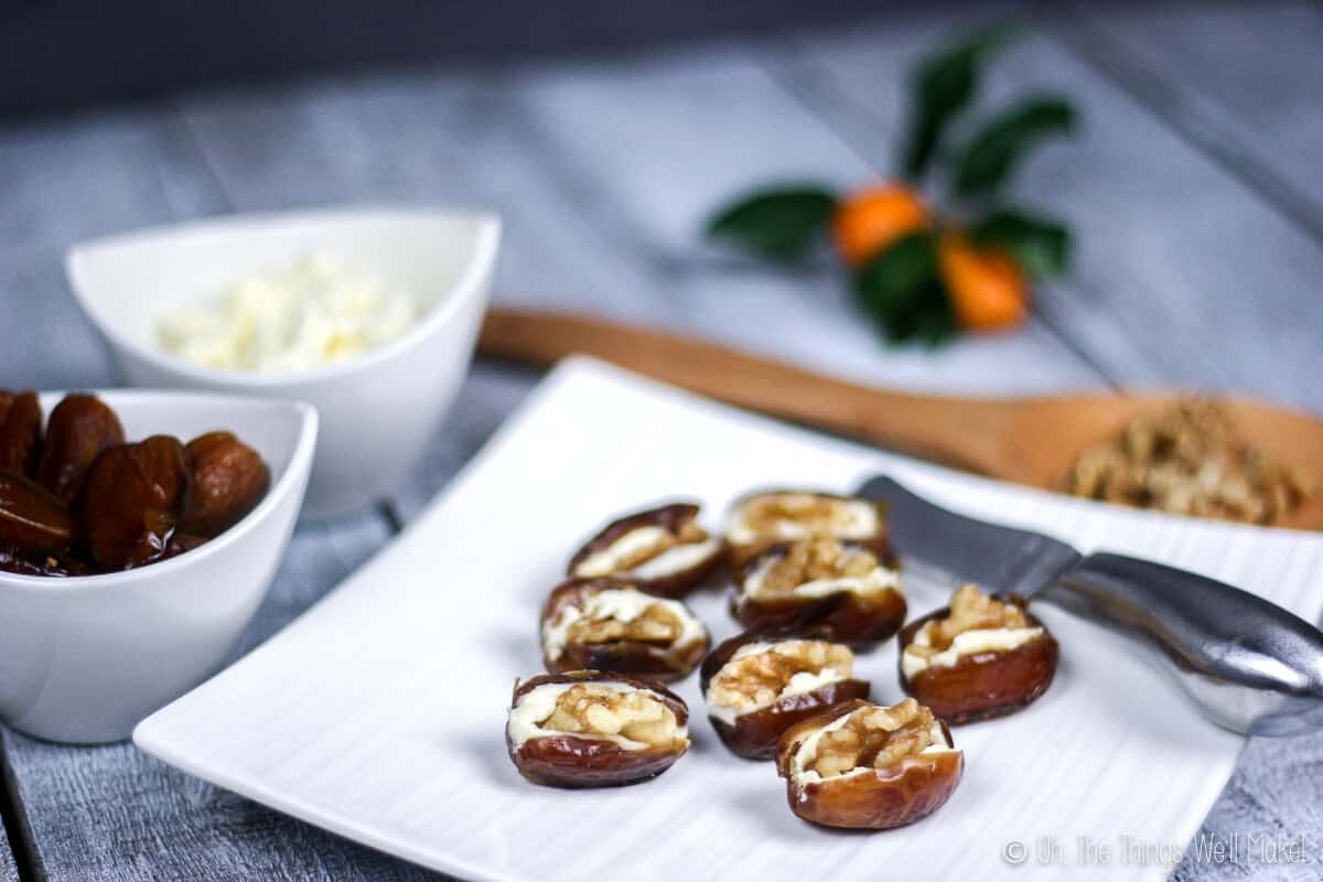 Close up of eight dates stuffed with cream cheese and topped with walnuts on a plate.