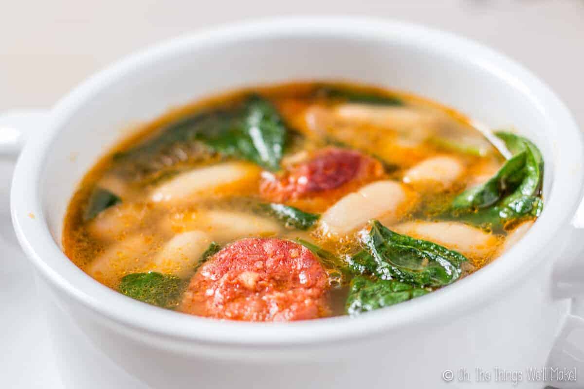 closeup of a bowl of white bean and chorizo soup with spinach, highlighting the ingredients.