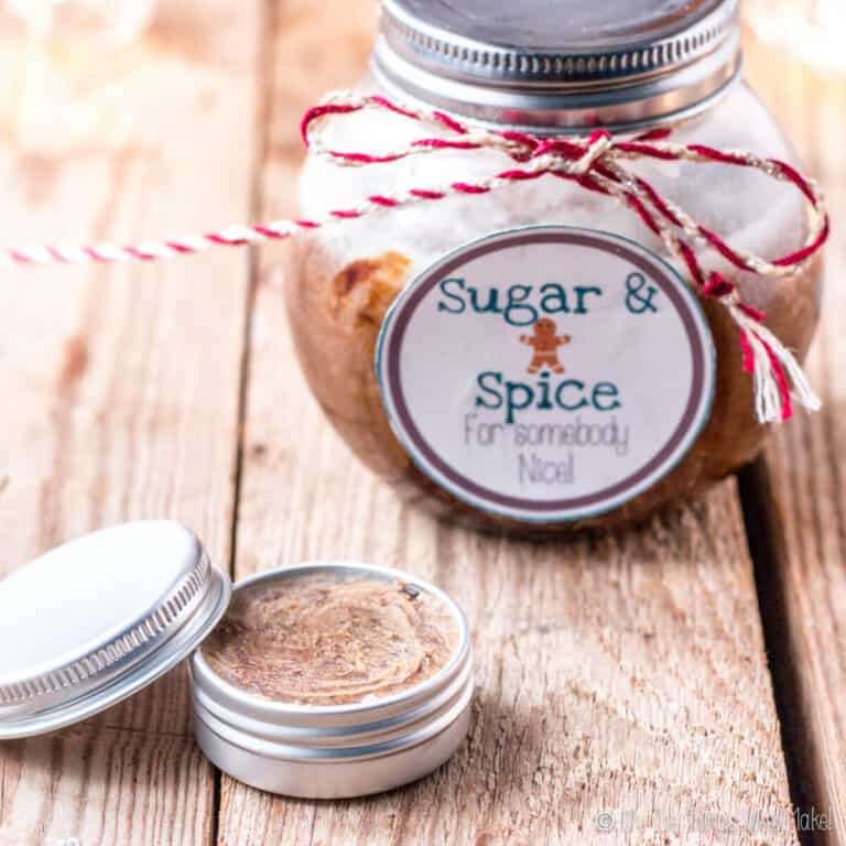 A closeup of a homemade sugar lip scrub in a small aluminum tin in front of a homemade sugar body scrub.