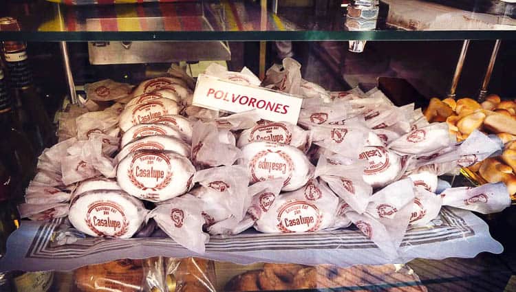 kasa käärittyjä polvorones-keksejä tarjottimella leipomon ikkunassa.