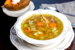 Overhead view of a turkey soup with celery, carrots, and turkey pieces in view. A baked sweet potato can be seen in the background.