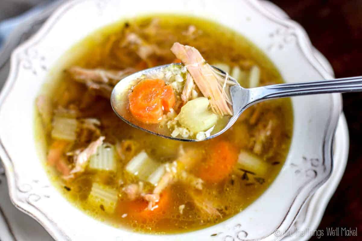 closeup view of spoon with turkey, carrot slice and celery over bowl of turkey rice soup