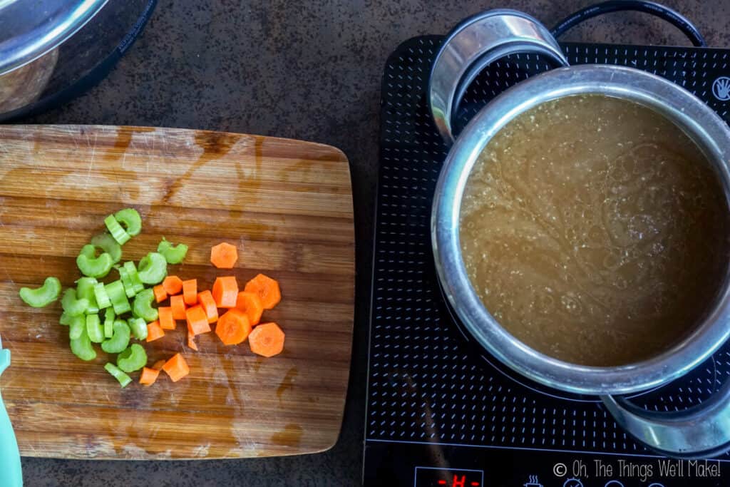 Overhead view of sliced celery and carrots next to a pot of turkey stock