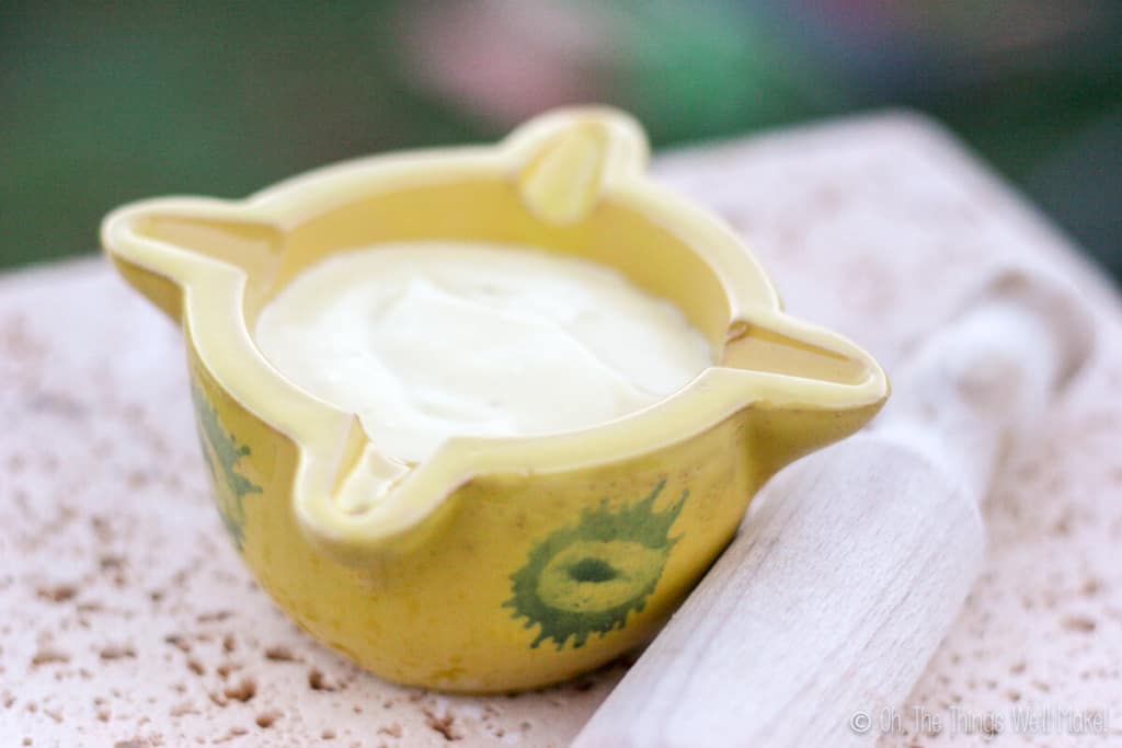 Homemade aioli in a yellow mortar with a wooden pestle to the side.