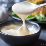 Pouring homemade aioli off the spoon to show its texture.