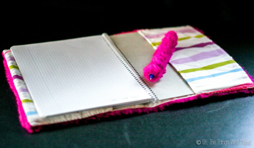 An open notebook with a cloth cover on it. A cloth wrapped pen is sitting on the notebook.