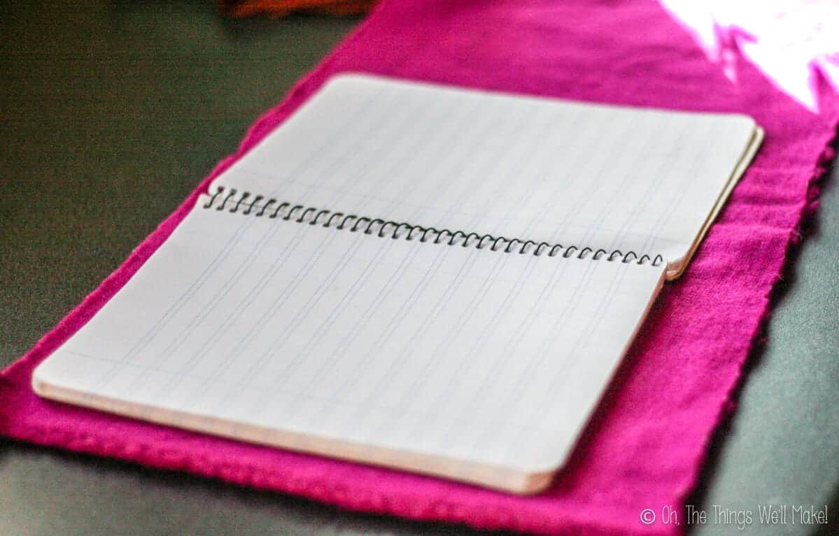 An open notebook sitting on a piece of pink cloth.