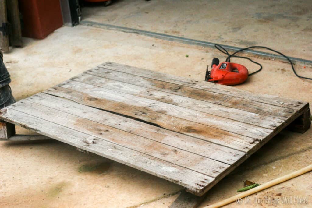 A wooden pallet on the ground with a jigsaw behind it.