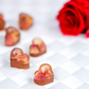 Close up of heart-shaped gummy treats with real rose petals inside next to a red rose.
