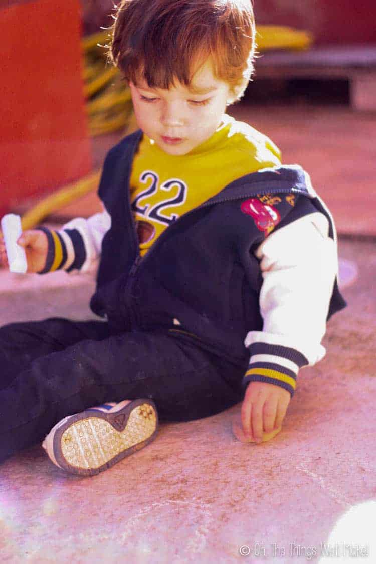 A small boy playing with homemade sidewalk chalk outside.