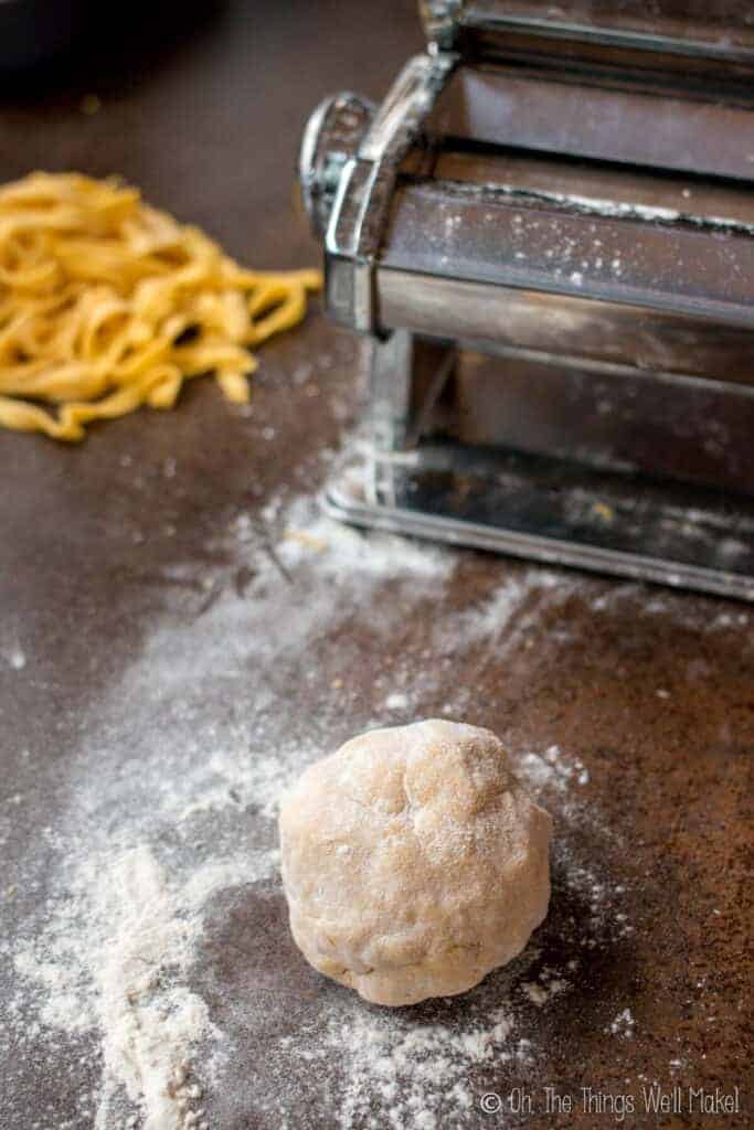 A ball of homemade pasta dough covered in flour and ready to be run through the pasta machine