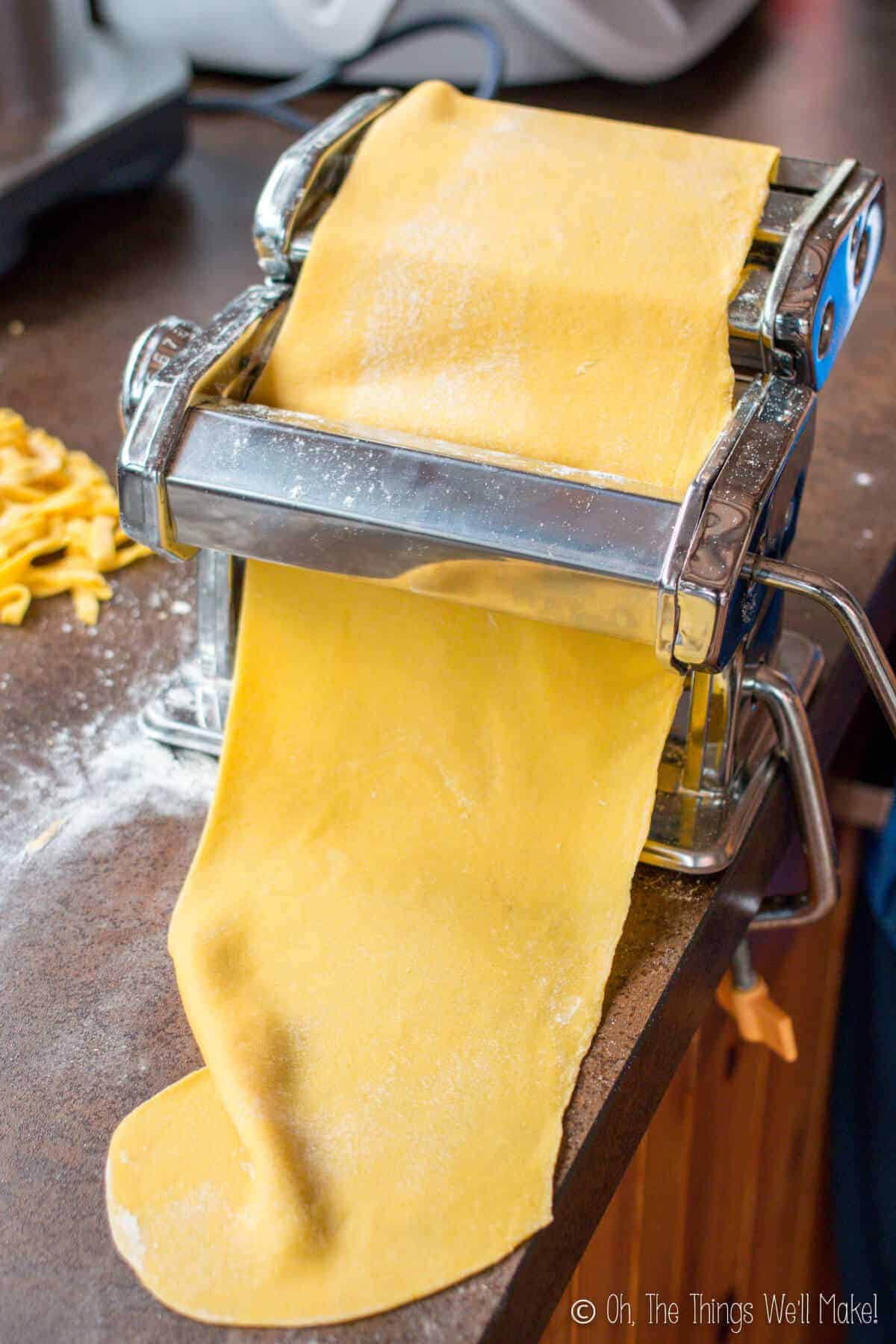 Running the pasta through a pasta maker to help flatten it out and make think sheets ready for cutting into fettuccine.